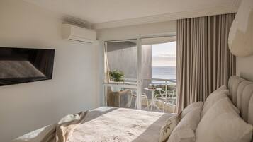 A hotel room with a bed, a TV, a balcony with a table and chairs, and a view of the sea.