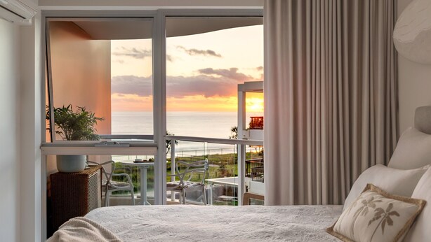 Una camera da letto con un'ampia finestra che si affaccia su un balcone e sul mare.