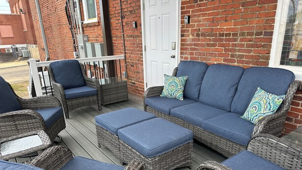 A covered outdoor seating area with wicker furniture and blue cushions, a white door, and a brick wall. - Charming 2 BR/2 bath in Historic District - Rent 1 Suite or Both/8-16 people! (Troy)