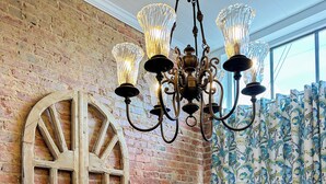 A dining area with a brick wall, a wooden table, white chairs, a chandelier, and a window with curtains. - Charming 2 BR/2 bath in Historic District - Rent 1 Suite or Both/8-16 people! (Troy)