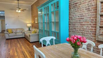 Un salon doté d’un plancher en bois, d’un canapé beige, d’une commode turquoise et d’une table à manger agrémentée d’un vase de fleurs.
