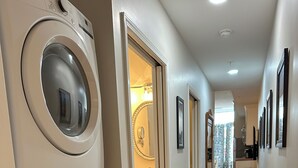 A laundry room with two stacked washers and dryers, a hallway leading to a bathroom, and a wooden floor. - Charming 2 BR/2 bath in Historic District - Rent 1 Suite or Both/8-16 people! (Troy)