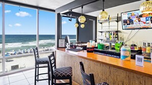 A bar with a view of the ocean, bar stools, a counter with a cash register, and a television displaying news.