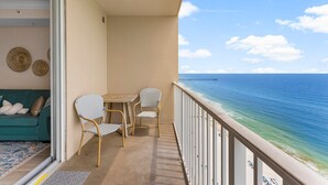 A balcony with a view of the ocean, a table, two chairs, and a green sofa.