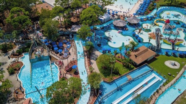 An aerial view of a resort with multiple swimming pools, water slides, and a beach area.