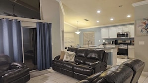A living room with a sofa, a dining table, and a kitchen area with appliances.