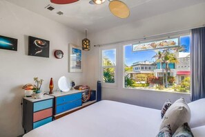 A bedroom with a bed, a dresser, a window with a view of buildings, and a ceiling light. - The Jetson House - 2 BD duplex top unit ocean view (San Diego)