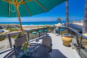 A balcony with outdoor seating, a large vase, and a view of the ocean.