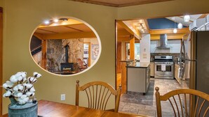 A dining area with a round mirror reflecting a stone fireplace, a wooden dining table, and chairs.