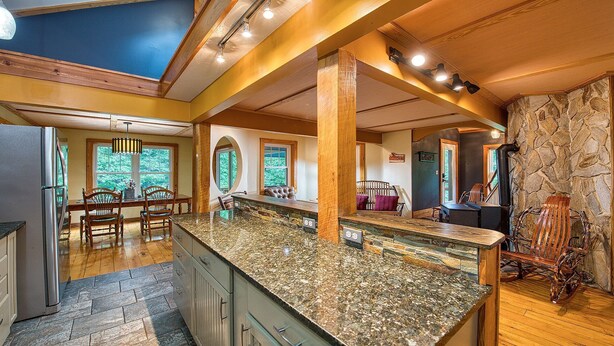 A spacious kitchen with granite countertops, wooden beams, and large windows offering views of the outdoors.