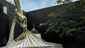 A macrame hammock hanging in a modern outdoor space with a concrete floor and dark walls.