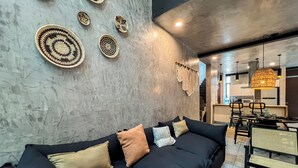 A modern living room with a dark sofa, a coffee table, and a dining area with chairs and a table.