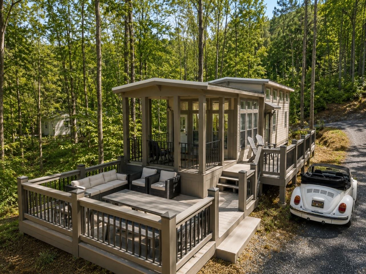 Eine Holzhütte mit Terrasse, Sitzgelegenheit im Freien und einem in der Nähe geparkten Oldtimer.
