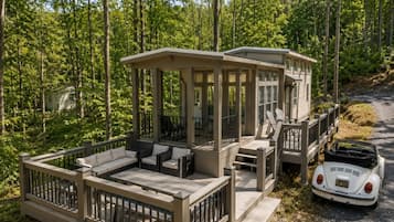Eine Holzhütte mit Terrasse, Sitzgelegenheit im Freien und einem in der Nähe geparkten Oldtimer.