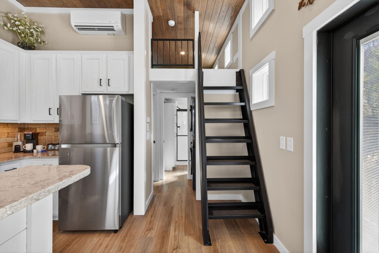 Une cuisine moderne avec un réfrigérateur en acier inoxydable, des armoires blanches et un plancher en bois.