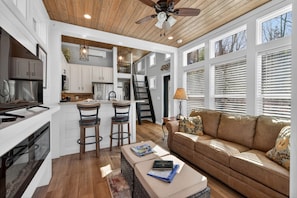 A modern kitchen with white cabinetry, a wooden ceiling, and a dining area with two bar stools. - Pet Friendly Tiny Home Retreat Near Blue Ridge (Blairsville)