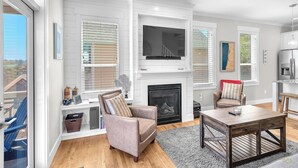 A modern living room with a fireplace, a television, and a dining area. - Sand Seeker in Olivia Beach (Lincoln City)