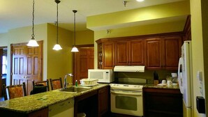 A kitchen with wooden cabinets, a granite countertop, a stove, a microwave, and pendant lights.
