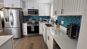 A modern kitchen with white cabinetry, stainless steel appliances, a blue tiled backsplash, and a wine rack. - Charming 2-bedroom house with WiFi, AC in beautiful Treasure Island (Treasure Island)