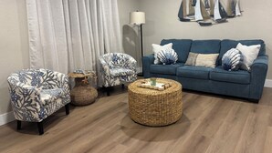 A living room with a blue sofa, two patterned armchairs, a round wicker coffee table, and a wall-mounted sailboat decoration. - Charming 2-bedroom house with WiFi, AC in beautiful Treasure Island (Treasure Island)