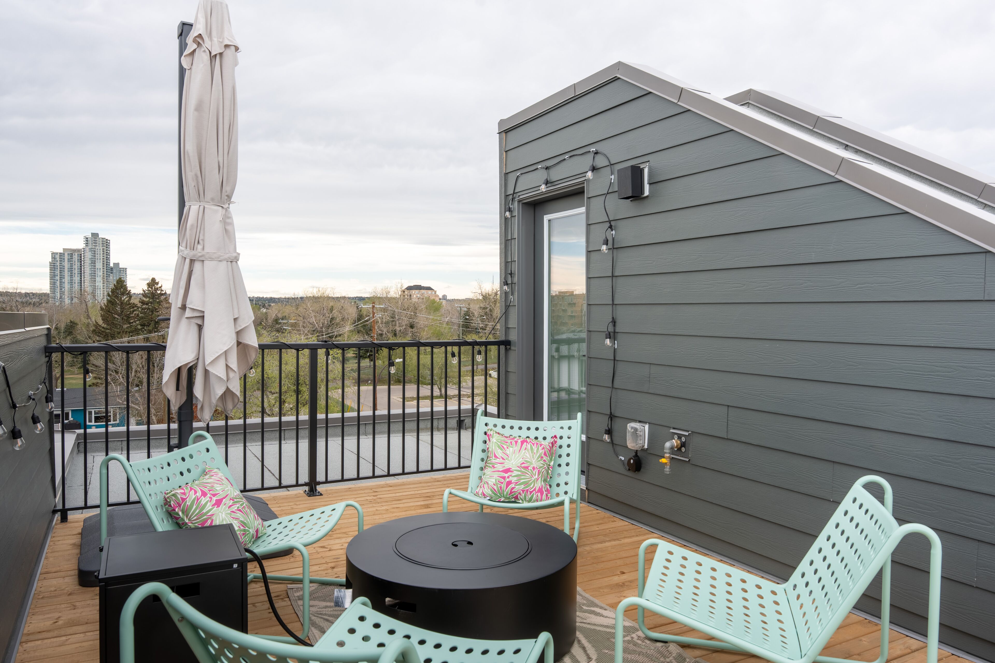 A rooftop deck with two green metal chairs, a round table, and a white umbrella.