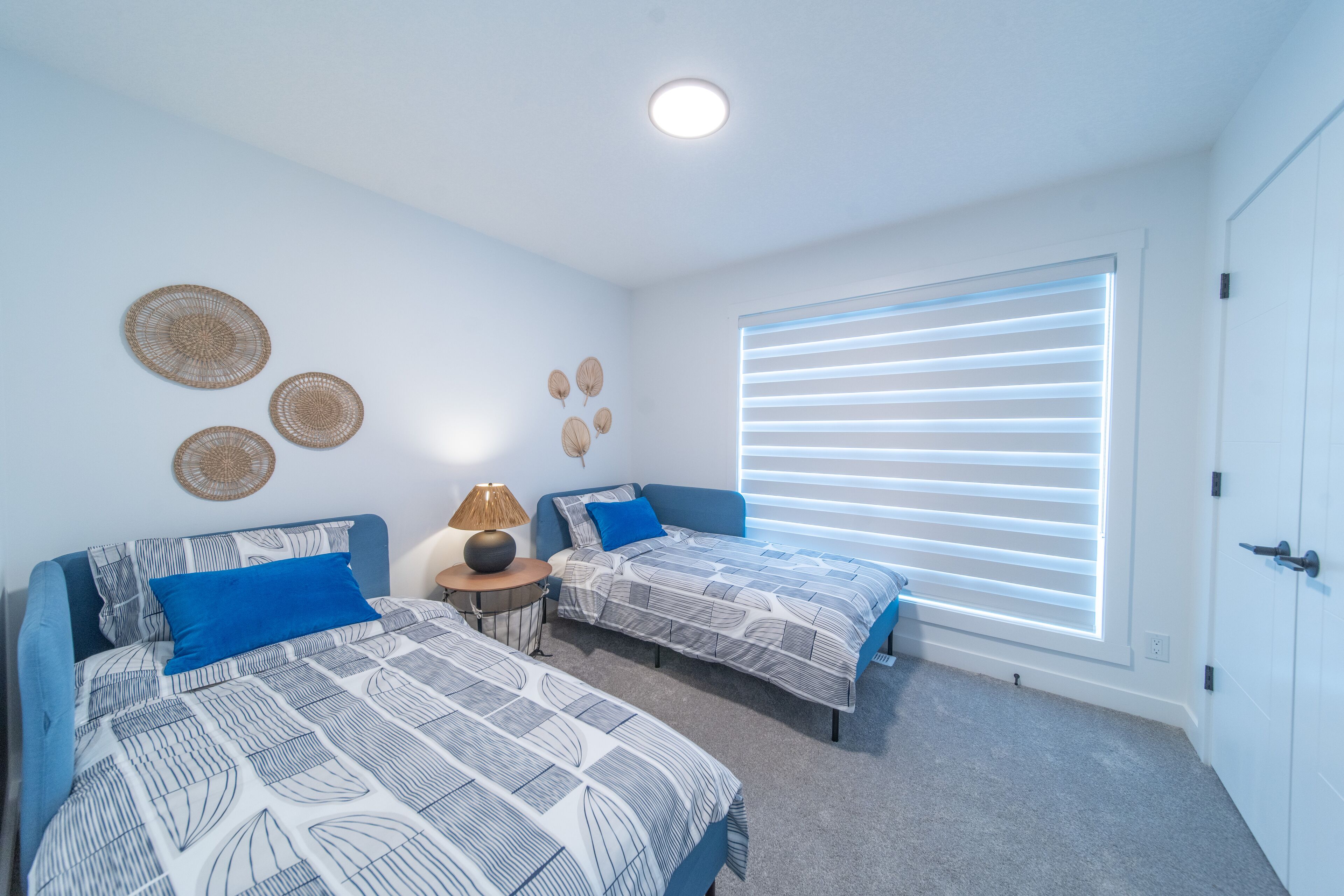 A bedroom with two beds, a window with blinds, a lamp, and wall decorations.