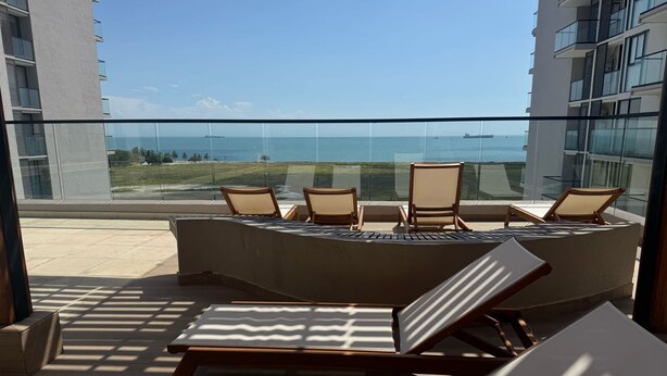 A sunlit outdoor seating area with lounge chairs and a table, overlooking a clear view of the ocean and distant ships. - Espectacular Apartament in Santa Marte (El Manantial)
