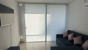 A modern living room with a dark-colored sofa, a flat-screen TV mounted on the wall, and a sliding glass door leading to a balcony. - Espectacular Apartament in Santa Marte (El Manantial)
