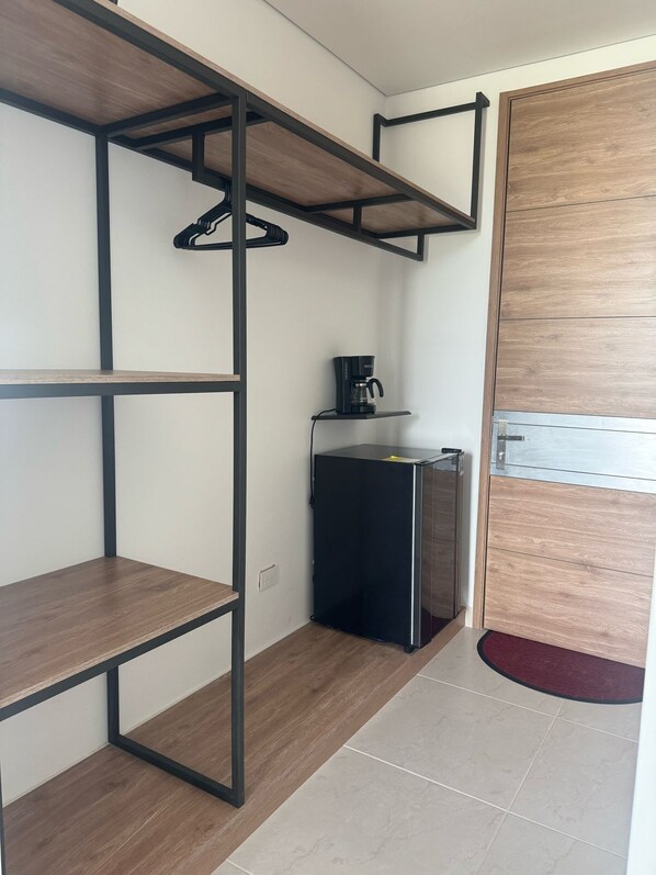 A room with a built-in wooden shelf unit, a small black refrigerator, and a coffee maker on a shelf.