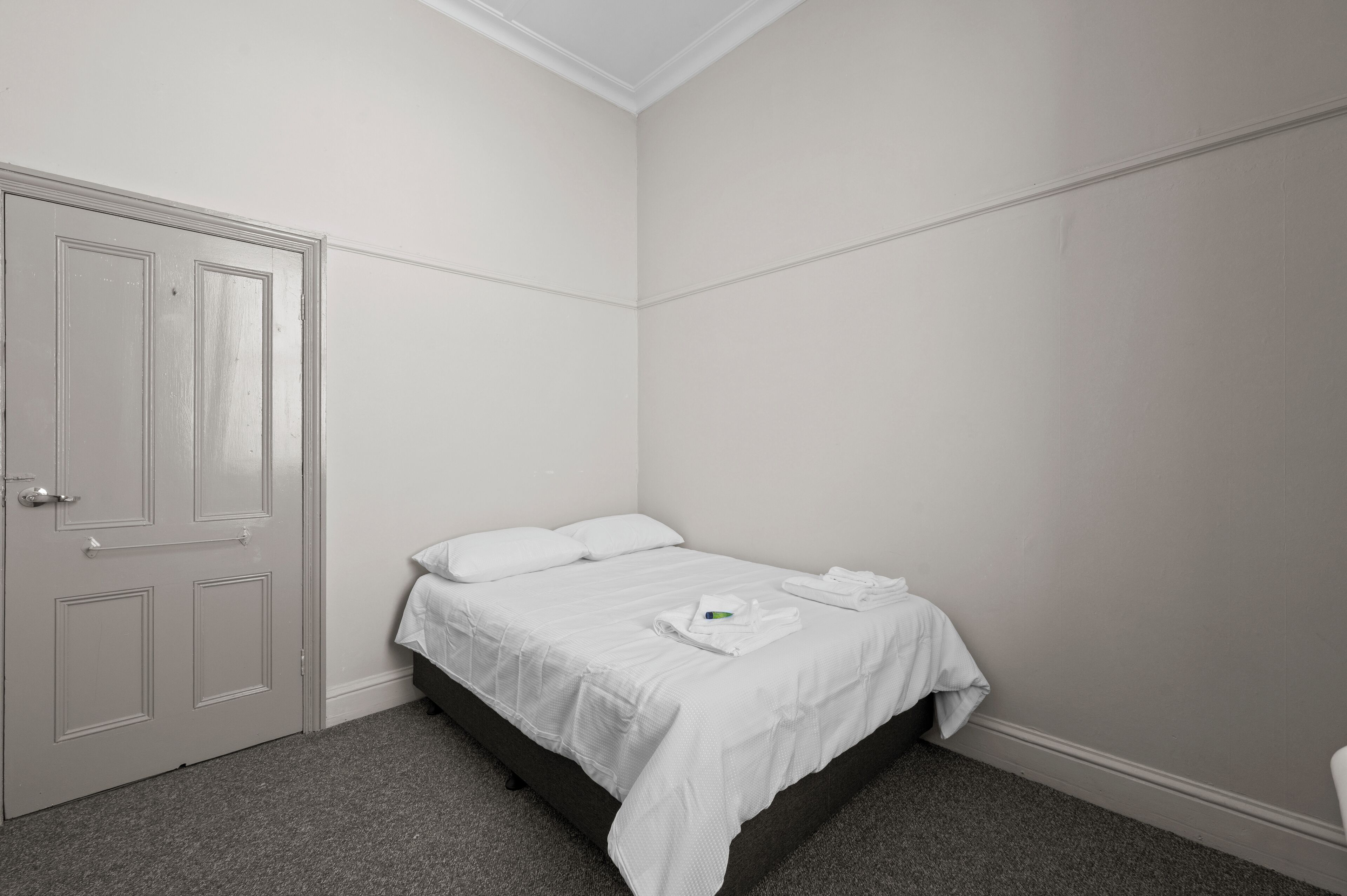 Une chambre avec un lit simple, une porte et un sol recouvert de moquette.