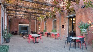 An outdoor patio area with brick walls, red and black chairs, and tables. - Euroa Hotel (Euroa)