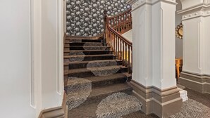 A grand staircase with ornate carpet runners and a wooden handrail, leading to a room with a patterned wallpaper and a large, ornate clock. - Euroa Hotel (Euroa)