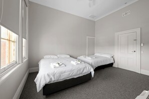 A hotel room with two beds, a window, a door, and a carpeted floor. - Euroa Hotel (Euroa)
