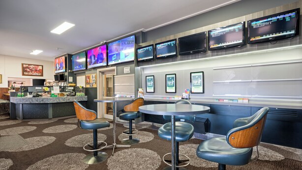 A modern bar area with multiple screens displaying content, bar stools, and a counter with a menu. - Euroa Hotel (Euroa)
