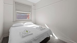 A hotel room with a bed, a window with blinds, a small table with a towel and a bottle, and a ceiling vent. - Euroa Hotel (Euroa)