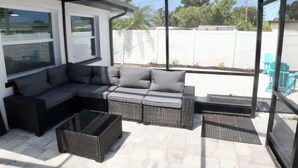 A covered patio with a sectional sofa, a glass coffee table, and a wicker chair. - Family 2BR Heated Pool Home with Fire Pit in Seminole (Seminole)