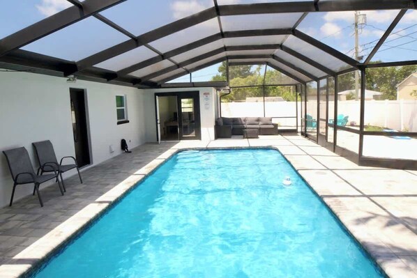 Une piscine couverte avec une structure en verre, un espace patio avec des chaises et une vue sur le jardin arrière.