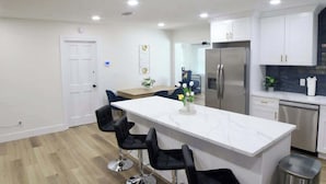 A modern kitchen with white cabinets, a stainless steel refrigerator, and a marble island with bar stools. - Family 2BR Heated Pool Home with Fire Pit in Seminole (Seminole)