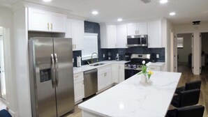 A modern kitchen with white cabinets, stainless steel appliances, and a marble island. - Family 2BR Heated Pool Home with Fire Pit in Seminole (Seminole)