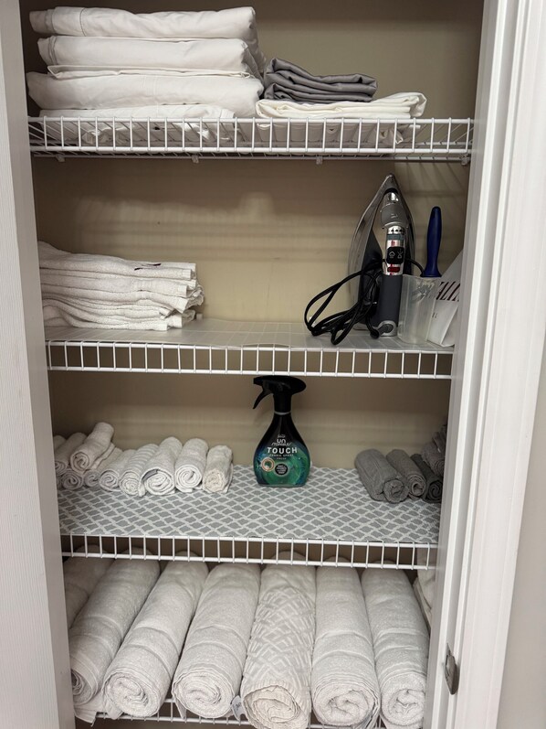 A storage closet with shelves holding folded towels and a spray bottle.