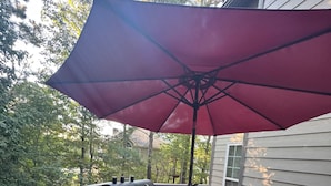 Una terraza con mesa de vidrio, sillas rojas y un gran paraguas rojo.