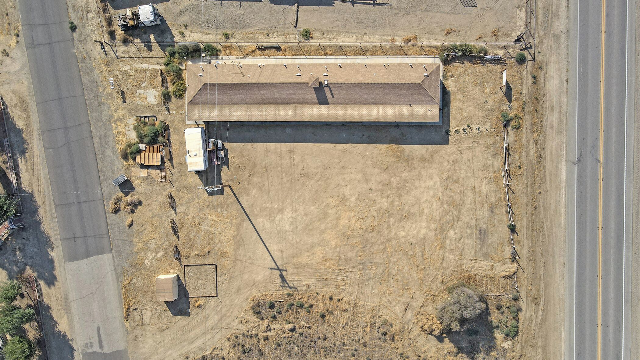 An aerial view of a building with a flat roof, surrounded by a fenced area and a dirt road.