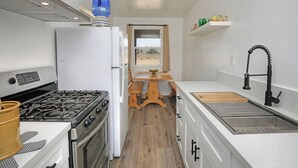 A compact kitchen with a gas stove, oven, white refrigerator, wooden table, and a window with a view.
