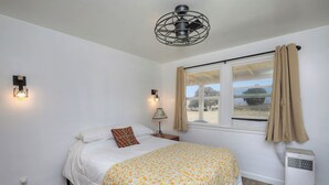 A bedroom with a bed, a window with curtains, a standing heater, and two wall-mounted lights.