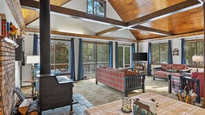 A spacious living room with a fireplace, large windows, and a cozy seating area. - Cozy 3-bedroom cabin on the Pere Marquette River (Baldwin)