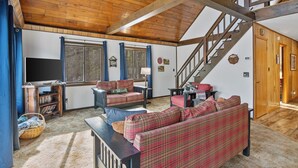 A spacious living room with a wooden ceiling, a staircase, and a large window. - Cozy 3-bedroom cabin on the Pere Marquette River (Baldwin)