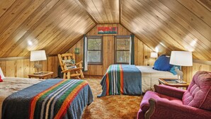 A cozy attic bedroom with wooden walls and sloped ceilings, featuring two beds, a rocking chair, and a plush armchair. - Cozy 3-bedroom cabin on the Pere Marquette River (Baldwin)