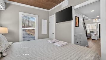 Un dormitorio con cama, televisor montado en la pared, ventana con persianas y una escalera que lleva a otra habitación.