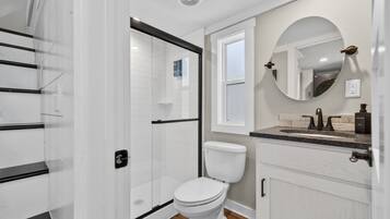 Un baño moderno con cabina de ducha de vidrio, inodoro blanco, tocador con lavabo y espejo.