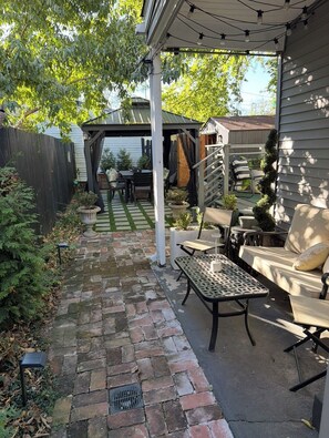 Een overdekt terras met een met stenen bestraat pad dat leidt naar buitenmeubels, waaronder een bank en stoelen.